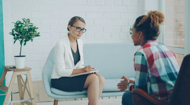 A therapist taking notes while talking with a client in a bright consulting room