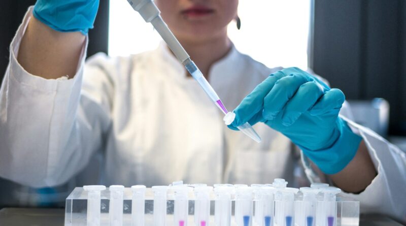 A researcher in blue gloves pipetting samples into test tubes in a laboratory