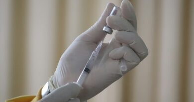Gloved hands drawing a vaccine dose from a vial into a syringe