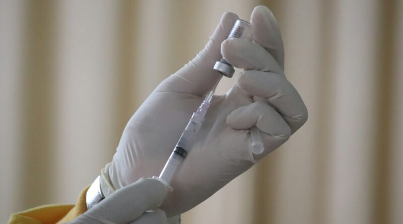 Gloved hands drawing a vaccine dose from a vial into a syringe