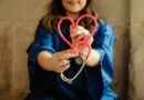 A healthcare worker in scrubs holding a pink stethoscope shaped like a heart
