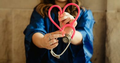 A healthcare worker in scrubs holding a pink stethoscope shaped like a heart