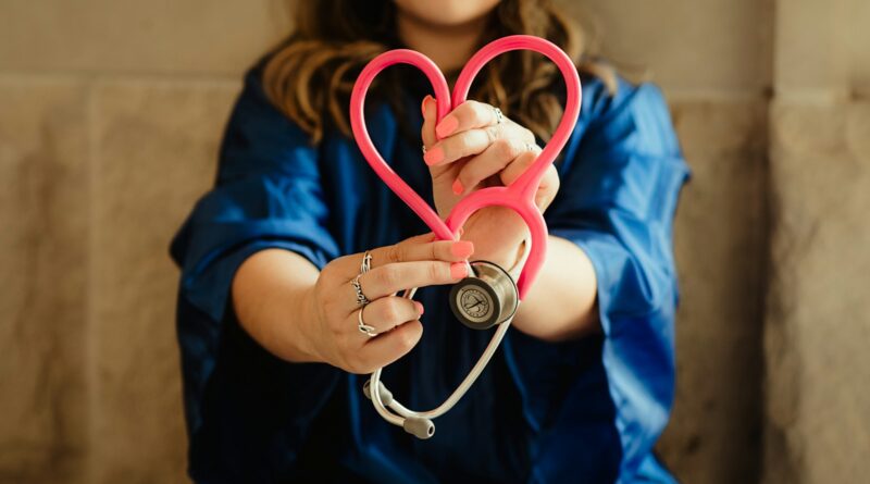 A healthcare worker in scrubs holding a pink stethoscope shaped like a heart